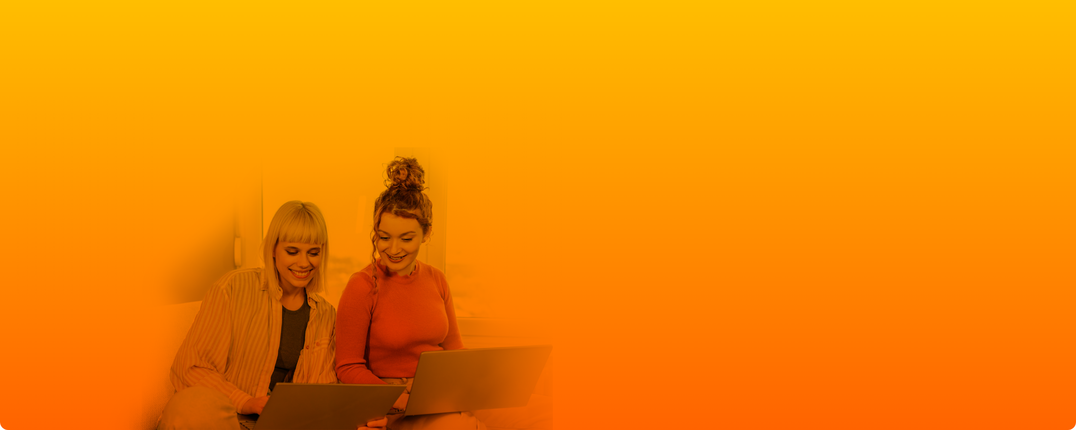 Zwei Frauen lächeln während sie auf den Laptop schauen.