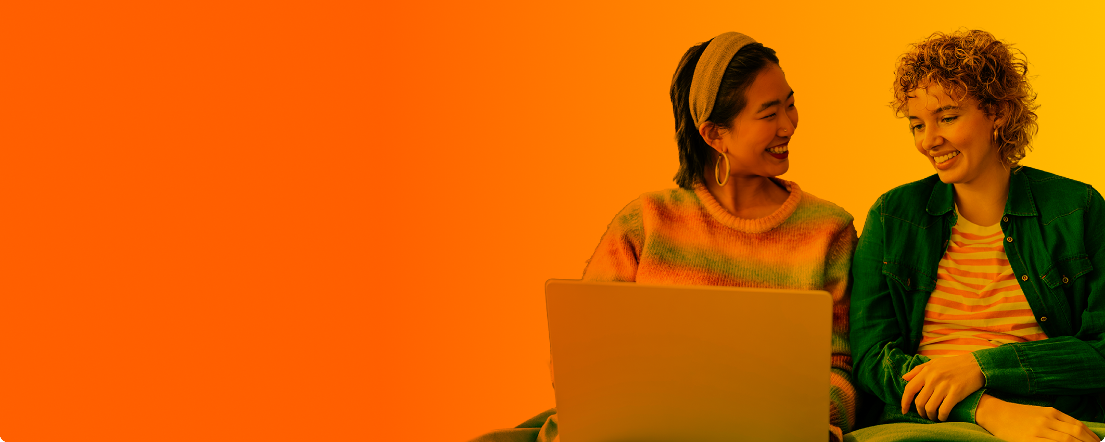 Zwei Frauen lächeln während sie auf den Laptop schauen.