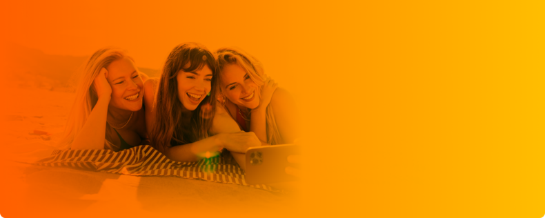 SIM-Karte Sommer-Deal: drei junge Frauen lächeln für ein Selfi auf einer Decke liegend in die Handykamera.