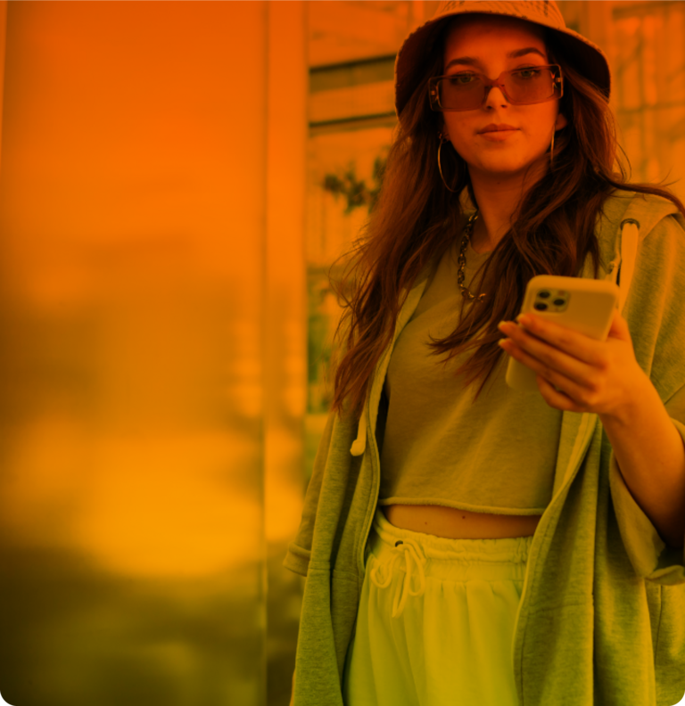 Eine junge Frau mit Sonnenbrille und Sonnenhut hält ihr Smartphone in der linken Hand und nutzt ihren Mobilfunktarif.