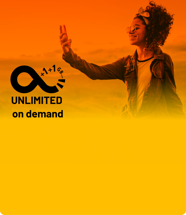 Fröhliche Frau macht sitzend ein Selfie in den Bergen und genießt ihren Tarif mit unbegrenztem Datenvolumen.