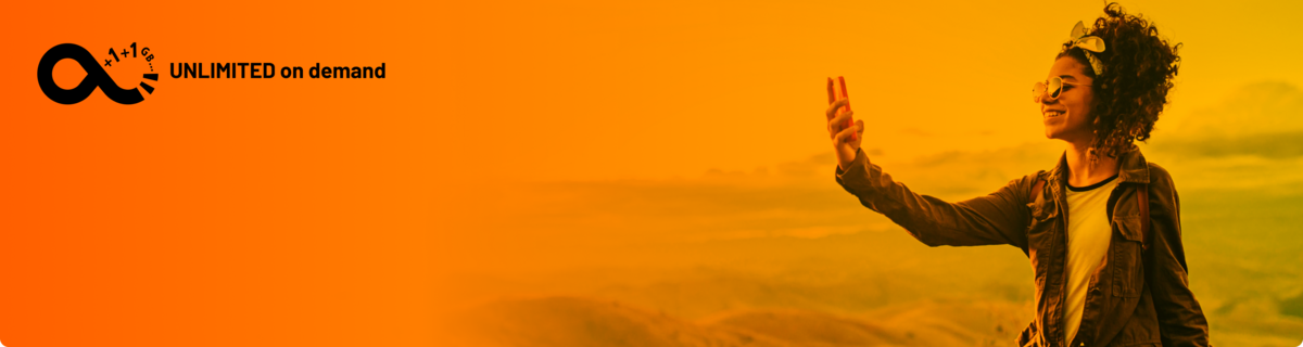 Fröhliche Frau macht sitzend ein Selfie in den Bergen und genießt ihren Tarif mit unbegrenztem Datenvolumen.