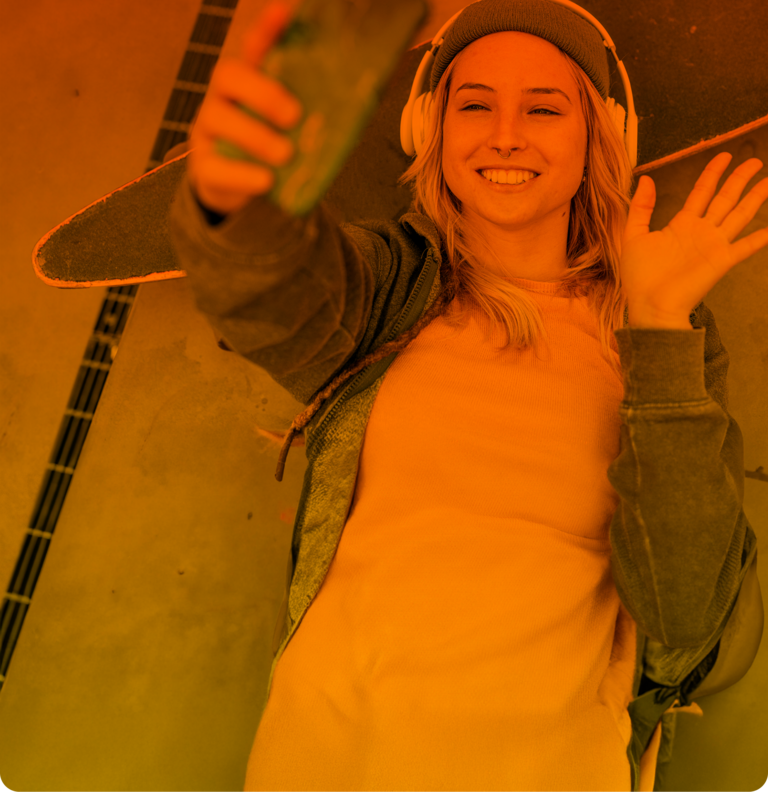 Eine junge Frau mit Kopfhörern liegt winkend auf ihrem Skateboard und telefoniert online, dank ihres Handytarifs.